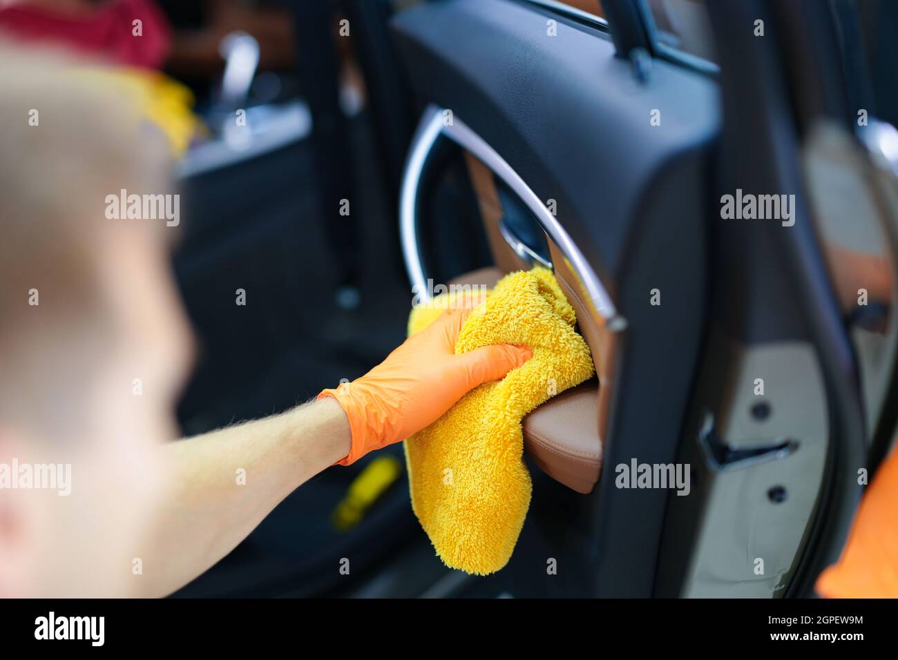 Mann in Gummihandschuhen, der mit einem Mikrofasertuch aus der Nähe Staub von der Autotür abwischt Stockfoto