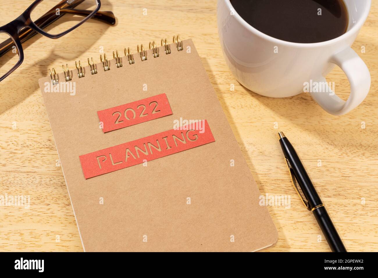 Planungskonzept für das neue Jahr 2022. Notizblock, Tasse Kaffee und Brille auf Holzschreibtisch Stockfoto