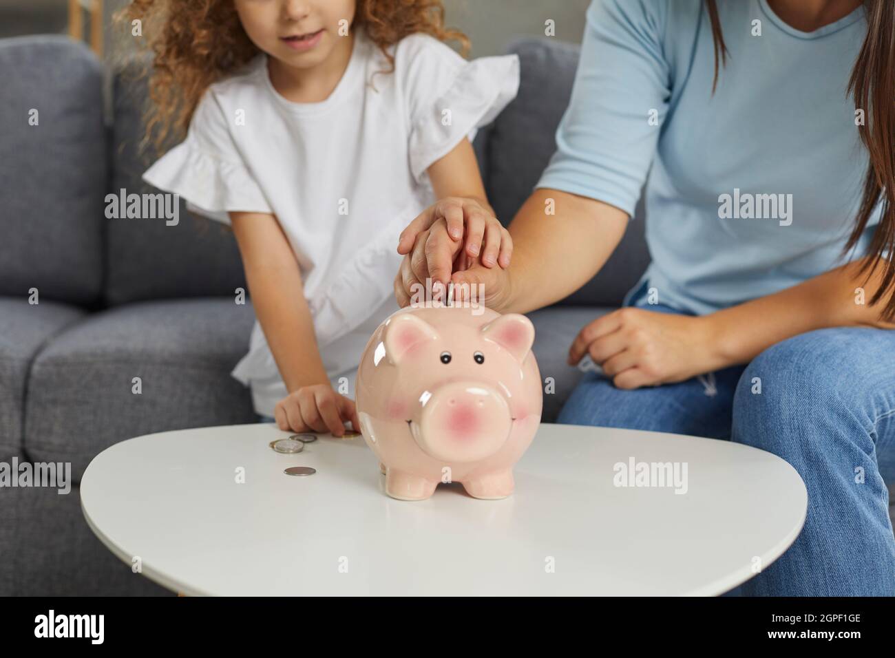 Mutter und Tochter, die planen, etwas Geld zu sparen, indem sie Münzen in Sparschwein stecken Stockfoto