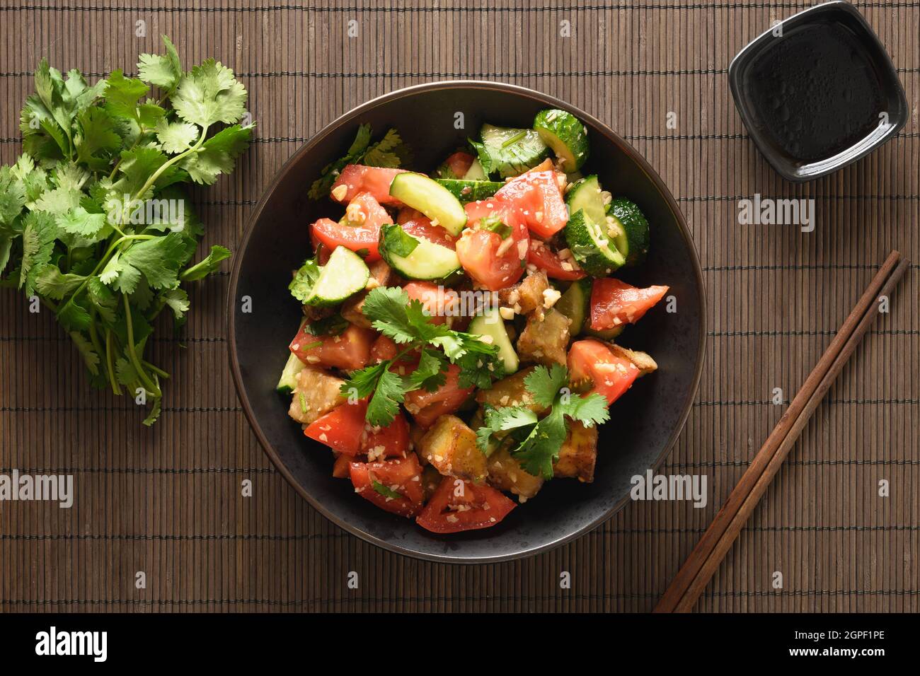Chinesische knusprige, würzige Aubergine mit Gurke, Knoblauch, Tomaten, frischen Koriander-Blättern in Austernsauce und schwarzem Essig auf schwarzem Hintergrund. Leckeres Kin Stockfoto