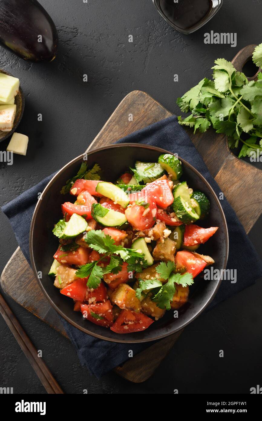 Chinesische knusprig-würzige braten Auberginen mit Gurken, Knoblauch, Tomaten, frischen Koriander-Blättern in Austernsauce und schwarzem Essig auf schwarzem Hintergrund. Anzeigen Stockfoto