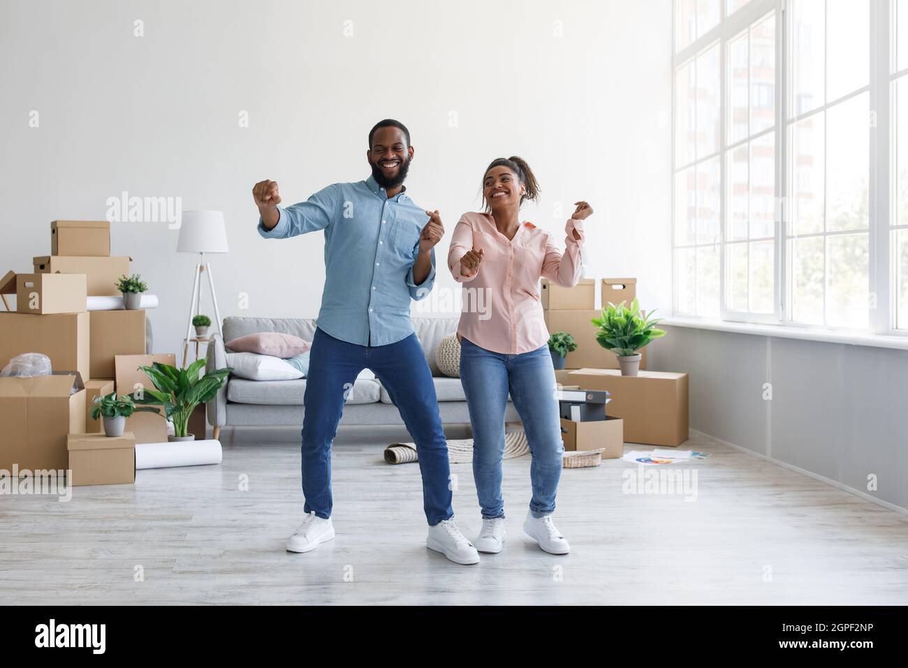 Zufriedenes junges afroamerikanisches Paar, das in der Wohnung mit Pappkartons im häuslichen Interieur tanzt, freier Raum Stockfoto