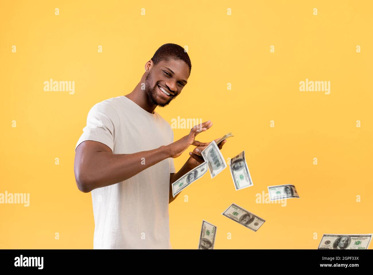 Big Win, Cashback, Wealth-Konzept. Junger afroamerikanischer Typ wirft Geldscheine aus, gelber Hintergrund Stockfoto