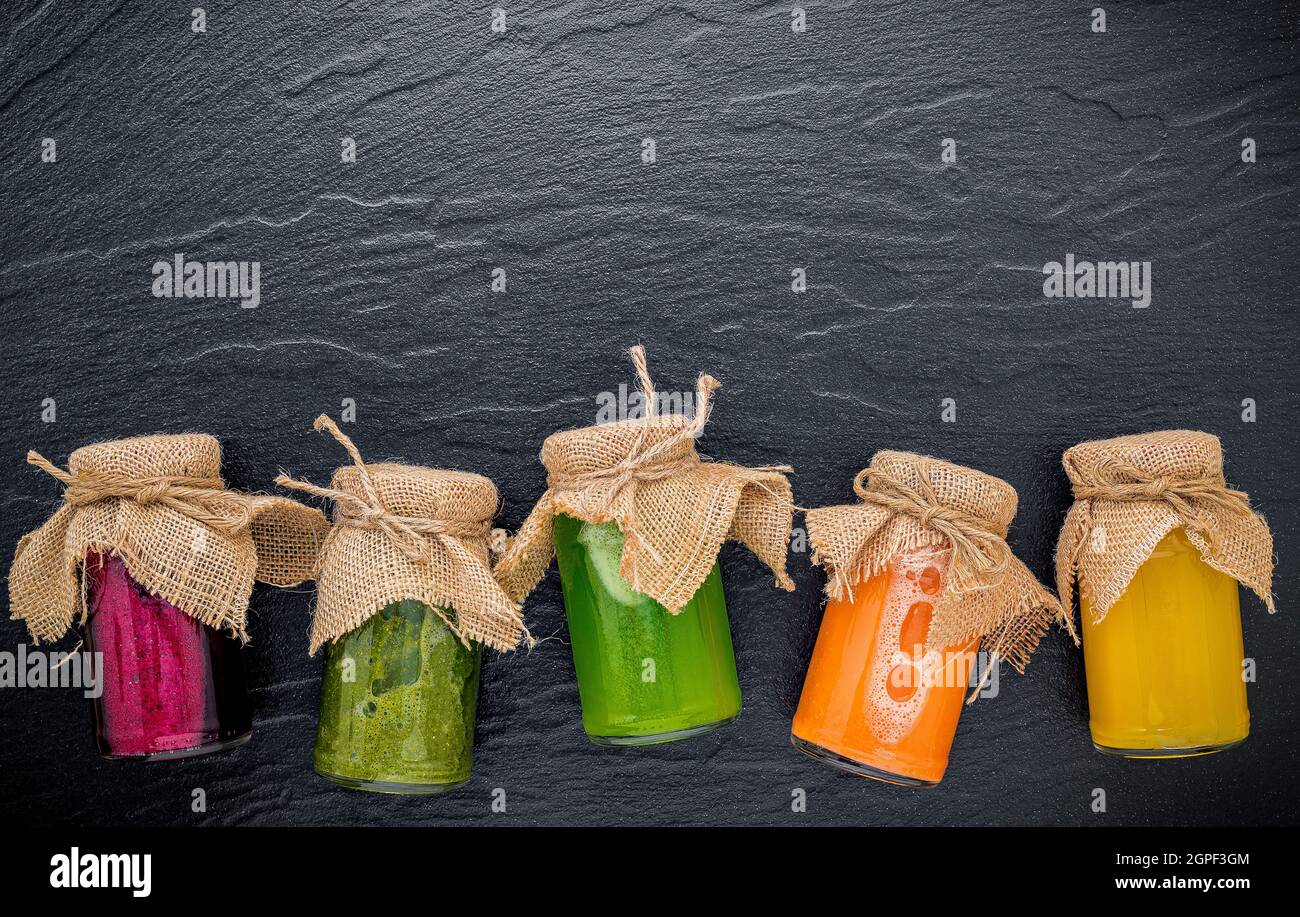 Bunte gesunde Smoothies und Säfte in Flaschen auf dunklem Stein Hintergrund mit kopieren. Stockfoto