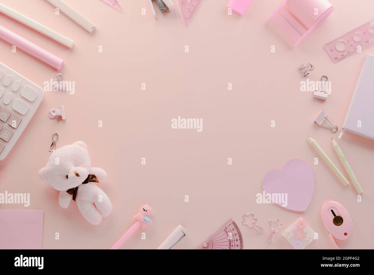 Draufsicht auf den femininen, weichen, in Pastellfarben gehaltenen Desktop-Arbeitsplatz, der aus Taschenrechner, Notizbuch, Stiften, Teddybär, Unterlage, stap Stockfoto