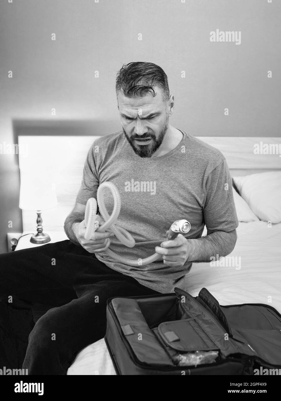 Unglücklich schockiert Mann mit chronischen Atemproblemen überrascht, indem CPAP-Maschine auf dem Bett im Schlafzimmer sitzen. Stockfoto