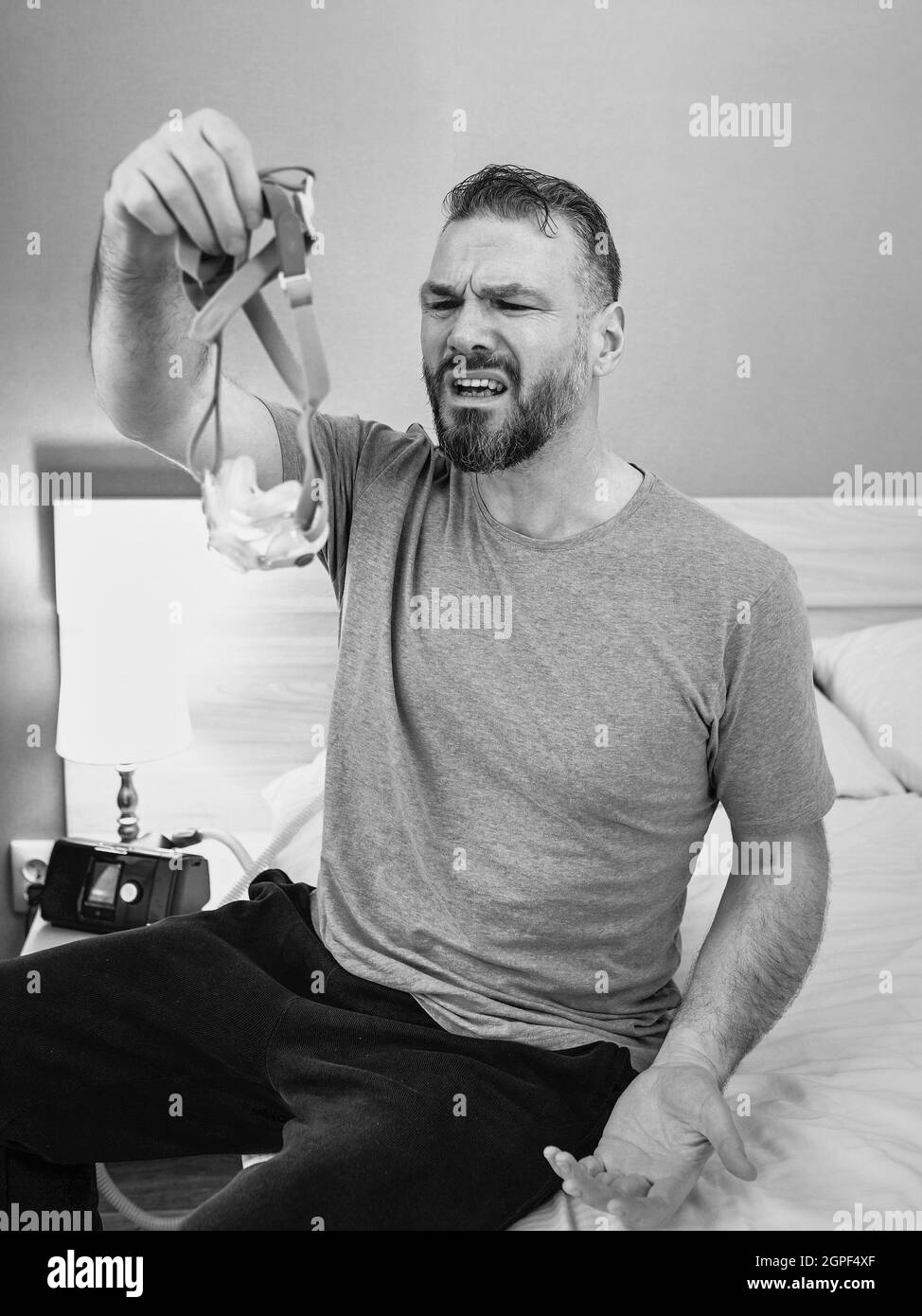 Unglücklich schockiert Mann mit chronischen Atemproblemen überrascht, indem CPAP-Maschine auf dem Bett im Schlafzimmer sitzen. Stockfoto
