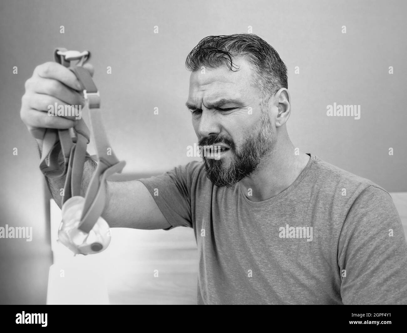 Unglücklich schockiert Mann mit chronischen Atemproblemen überrascht, indem CPAP-Maschine auf dem Bett im Schlafzimmer sitzen. Stockfoto