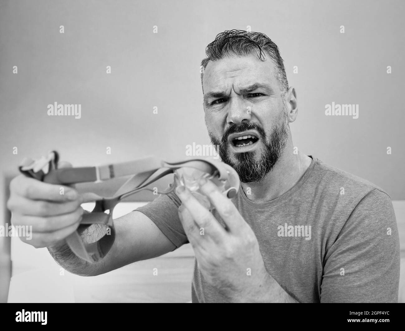Unglücklich schockiert Mann mit chronischen Atemproblemen überrascht, indem CPAP-Maschine auf dem Bett im Schlafzimmer sitzen. Stockfoto