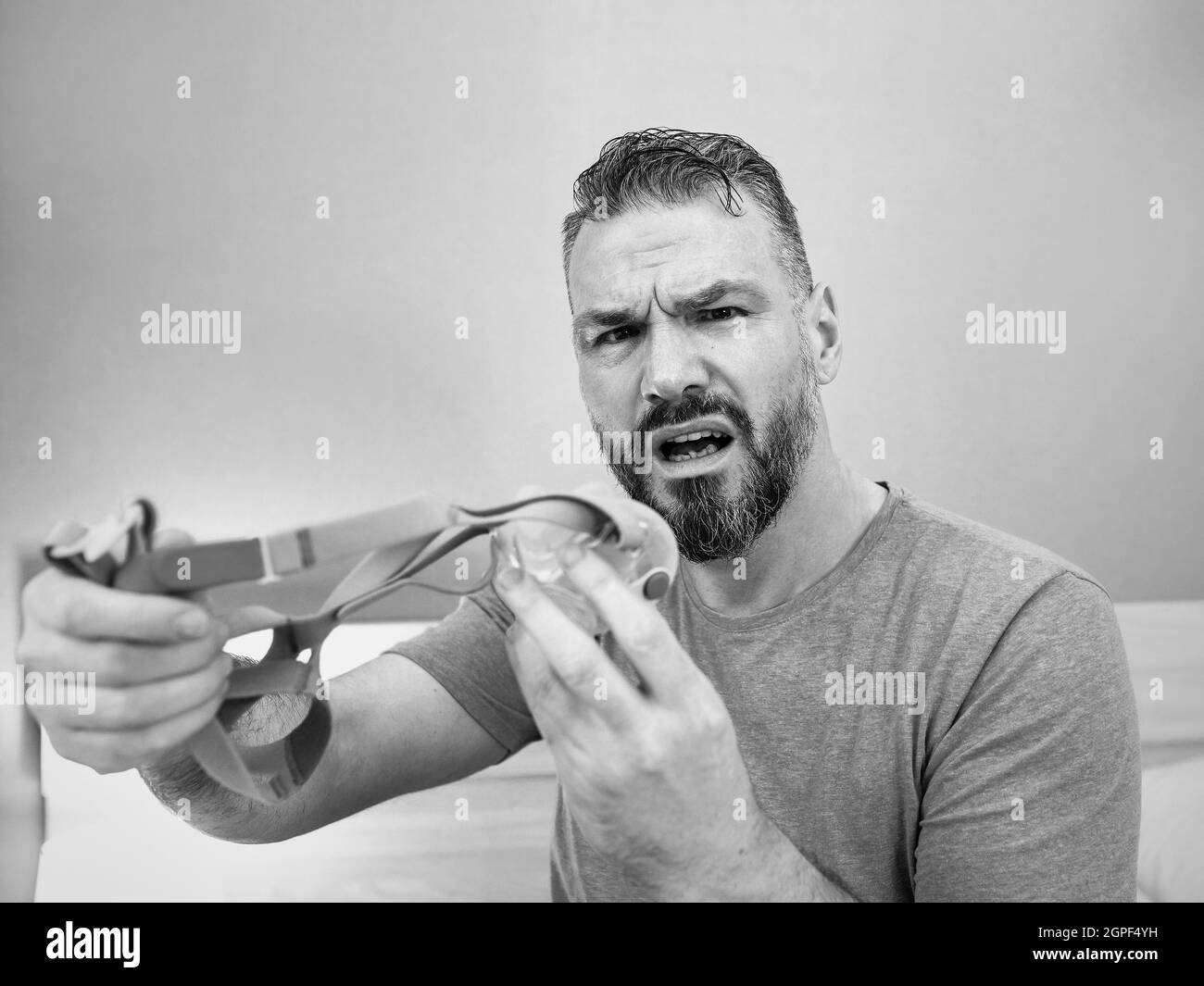 Unglücklich schockiert Mann mit chronischen Atemproblemen überrascht, indem CPAP-Maschine auf dem Bett im Schlafzimmer sitzen. Stockfoto