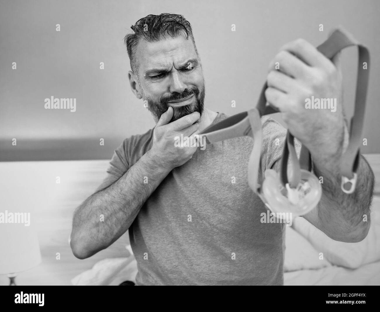 Unglücklich schockiert Mann mit chronischen Atemproblemen überrascht, indem CPAP-Maschine auf dem Bett im Schlafzimmer sitzen. Stockfoto