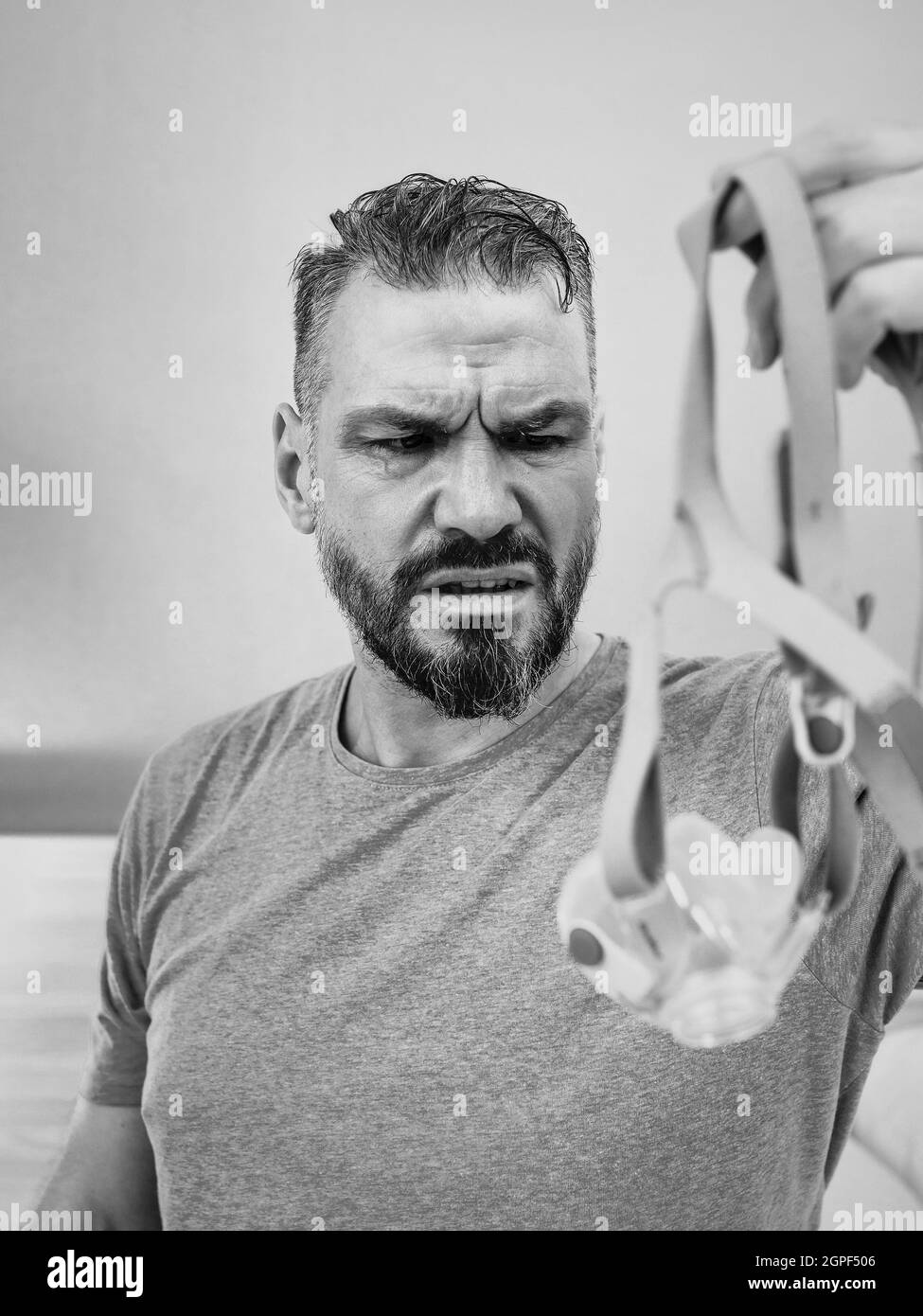 Unglücklich schockiert Mann mit chronischen Atemproblemen überrascht, indem CPAP-Maschine auf dem Bett im Schlafzimmer sitzen. Stockfoto