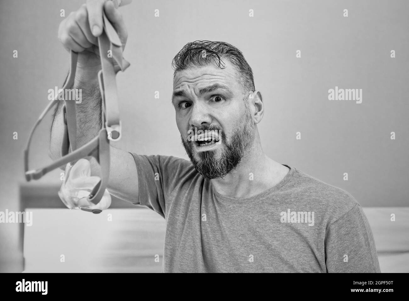 Unglücklich schockiert Mann mit chronischen Atemproblemen überrascht, indem CPAP-Maschine auf dem Bett im Schlafzimmer sitzen. Stockfoto