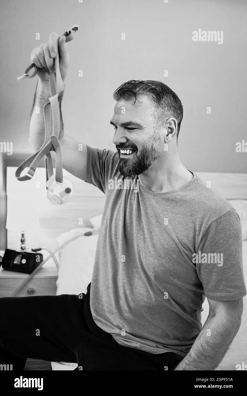 Unglücklich schockiert Mann mit chronischen Atemproblemen überrascht, indem CPAP-Maschine auf dem Bett im Schlafzimmer sitzen. Stockfoto