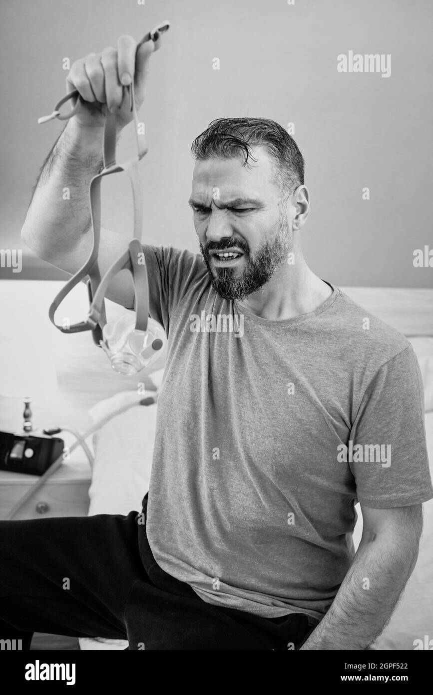 Unglücklich schockiert Mann mit chronischen Atemproblemen überrascht, indem CPAP-Maschine auf dem Bett im Schlafzimmer sitzen. Stockfoto