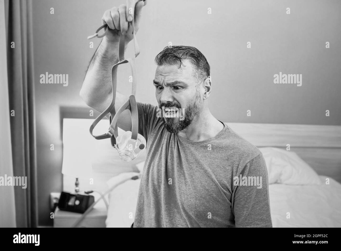 Unglücklich schockiert Mann mit chronischen Atemproblemen überrascht, indem CPAP-Maschine auf dem Bett im Schlafzimmer sitzen. Stockfoto