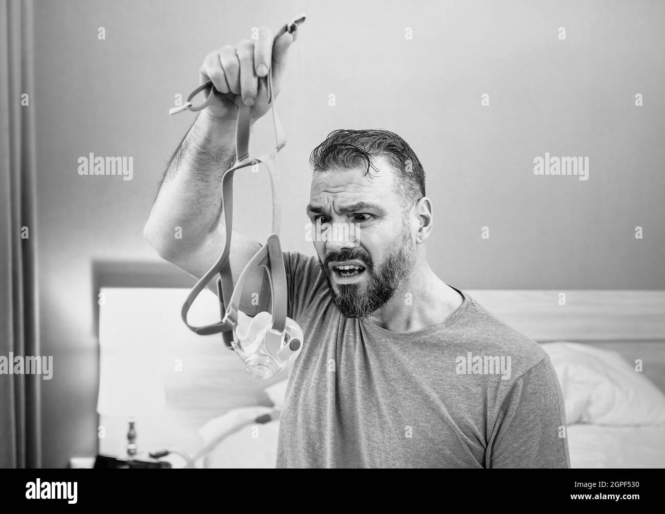 Unglücklich schockiert Mann mit chronischen Atemproblemen überrascht, indem CPAP-Maschine auf dem Bett im Schlafzimmer sitzen. Stockfoto