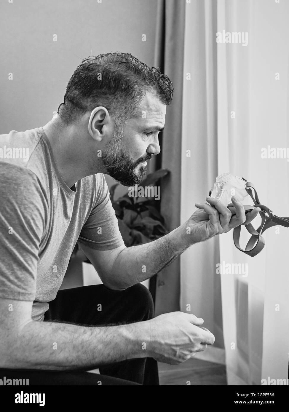 Monochromes Porträt eines glücklichen ausgeruhten Mannes mit chronischen Atemproblemen nach der Verwendung eines CPAP-Geräts, das im Schlafzimmer auf dem Bett sitzt. Gesundheitswesen, CPAP Stockfoto