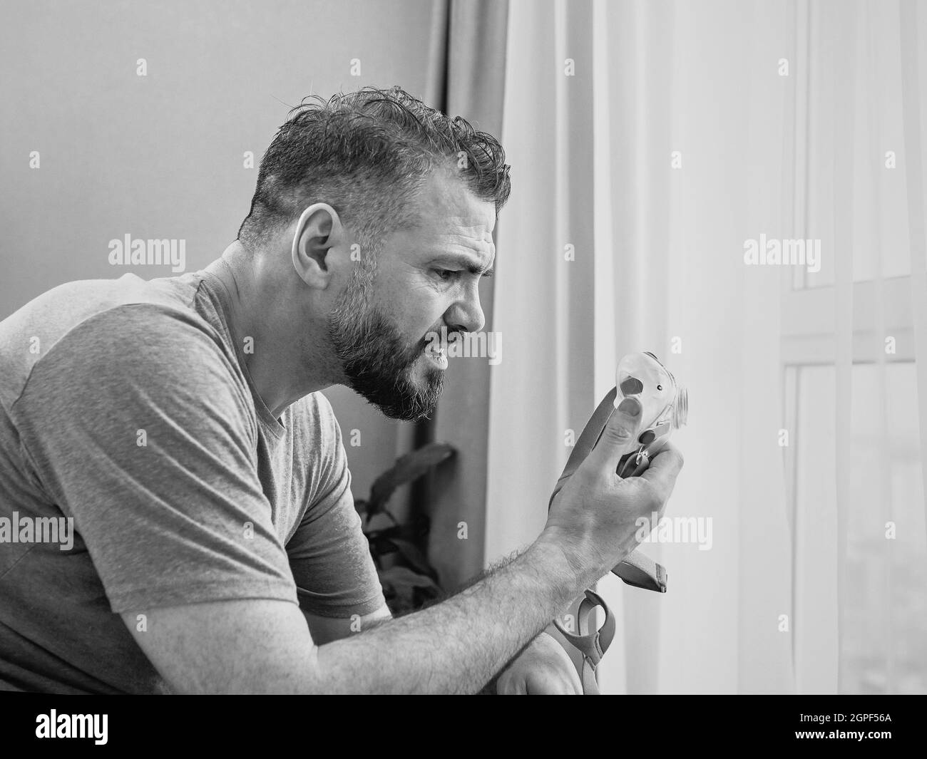 Reifer glücklicher Mann mit chronischen Atemproblemen erwägt die Verwendung CPAP-Maschine auf dem Bett im Schlafzimmer sitzen. Gesundheitswesen, CPAP, Schnarchen Konzept Stockfoto