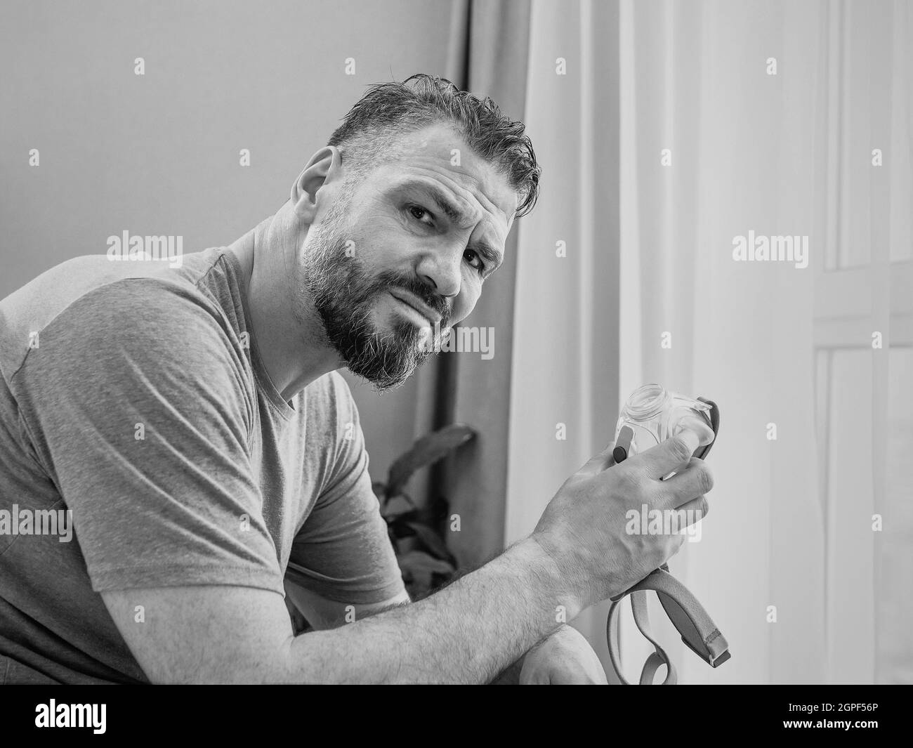 Reifer glücklicher Mann mit chronischen Atemproblemen erwägt die Verwendung CPAP-Maschine auf dem Bett im Schlafzimmer sitzen. Gesundheitswesen, CPAP, Schnarchen Konzept Stockfoto