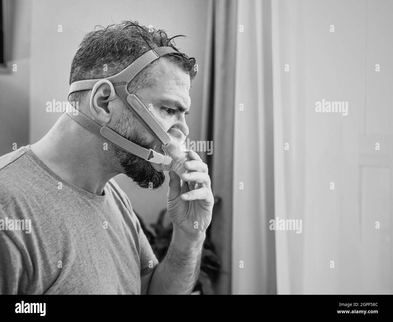 Unglücklich schockiert Mann mit chronischen Atemproblemen überrascht, indem CPAP-Maschine auf dem Bett im Schlafzimmer sitzen. Stockfoto