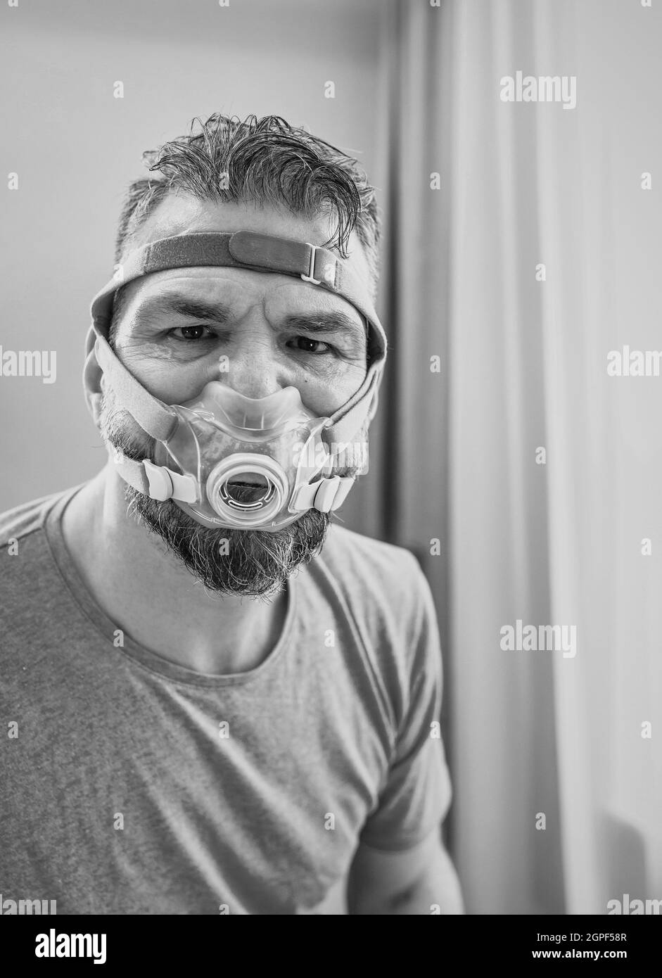 Unglücklich schockiert Mann mit chronischen Atemproblemen überrascht, indem CPAP-Maschine auf dem Bett im Schlafzimmer sitzen. Stockfoto