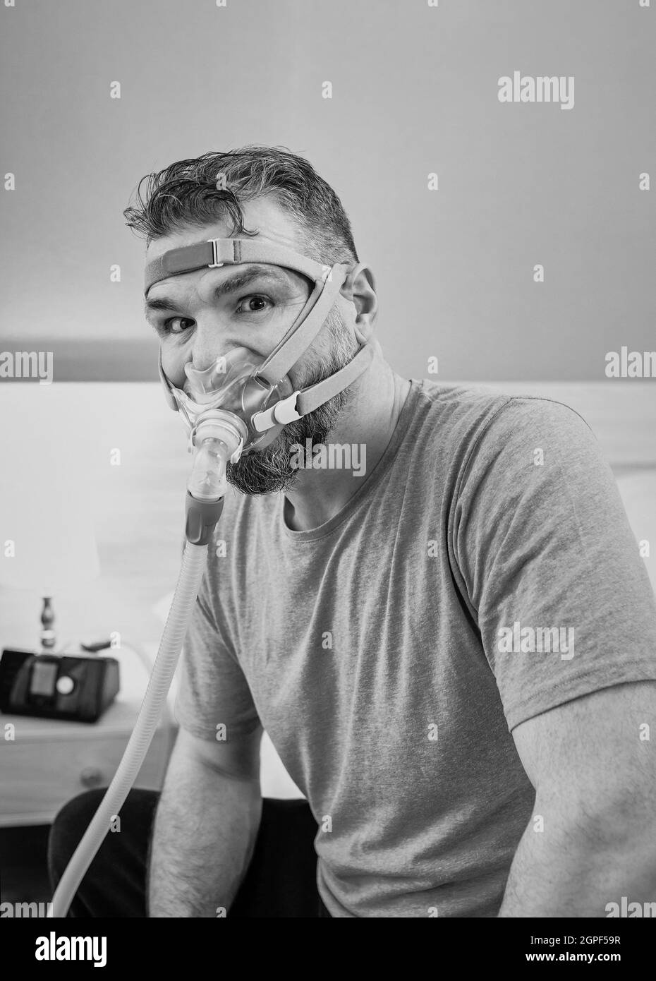 Unglücklich schockiert Mann mit chronischen Atemproblemen überrascht, indem CPAP-Maschine auf dem Bett im Schlafzimmer sitzen. Stockfoto