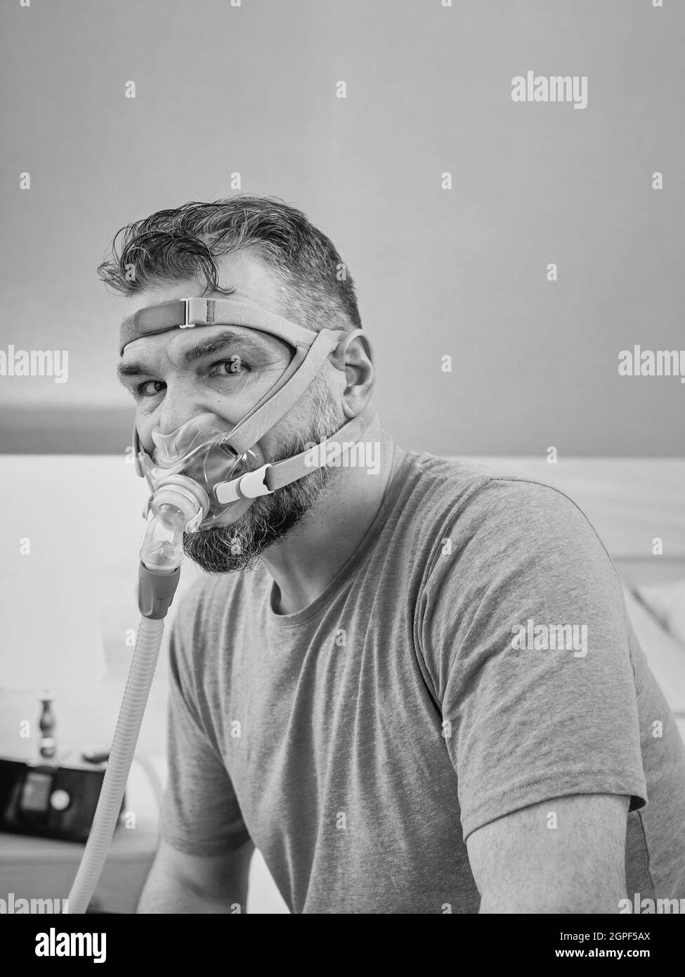 Unglücklich schockiert Mann mit chronischen Atemproblemen überrascht, indem CPAP-Maschine auf dem Bett im Schlafzimmer sitzen. Stockfoto