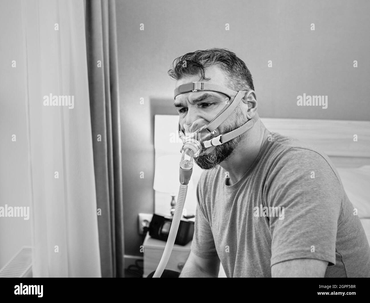 Unglücklich schockiert Mann mit chronischen Atemproblemen überrascht, indem CPAP-Maschine auf dem Bett im Schlafzimmer sitzen. Stockfoto