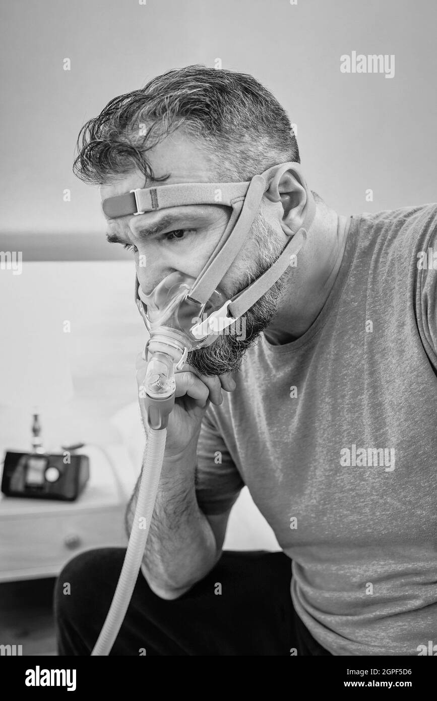 Unglücklich schockiert Mann mit chronischen Atemproblemen überrascht, indem CPAP-Maschine auf dem Bett im Schlafzimmer sitzen. Stockfoto