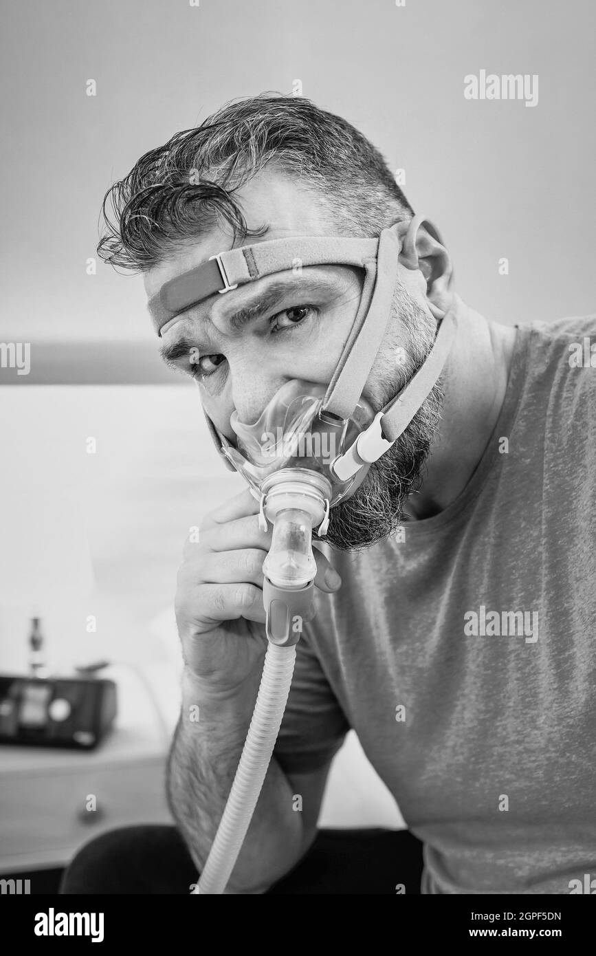 Unglücklich schockiert Mann mit chronischen Atemproblemen überrascht, indem CPAP-Maschine auf dem Bett im Schlafzimmer sitzen. Stockfoto