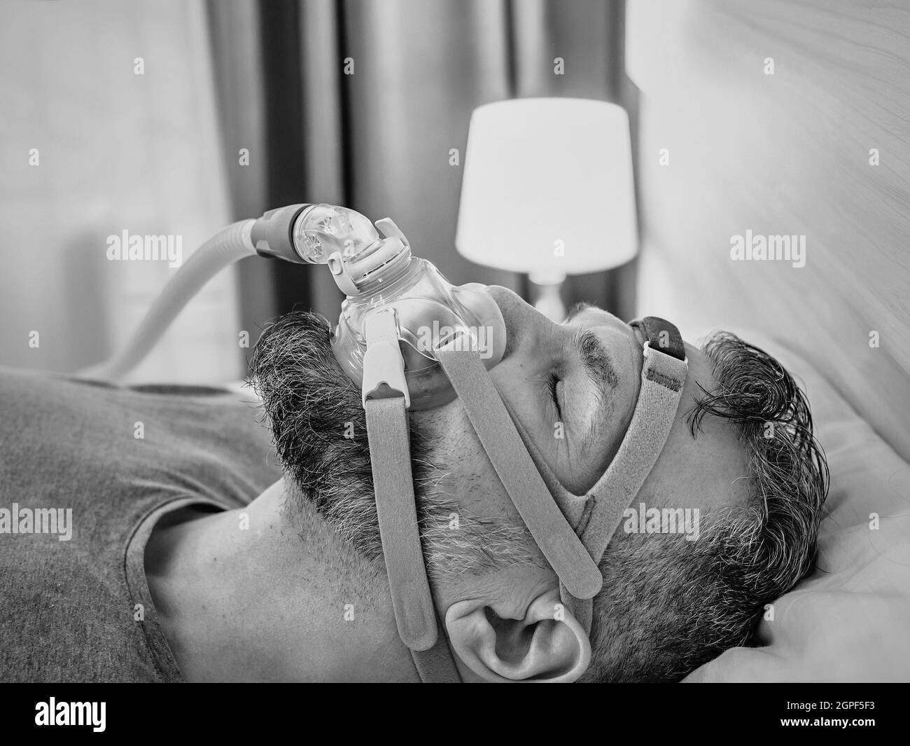 Monochromes Porträt eines schlafenden Mannes mit chronischen Atemproblemen erwägt die Verwendung des CPAP-Geräts im Bett. Gesundheitswesen, obstruktive Schlafapnoe-Therapie Stockfoto