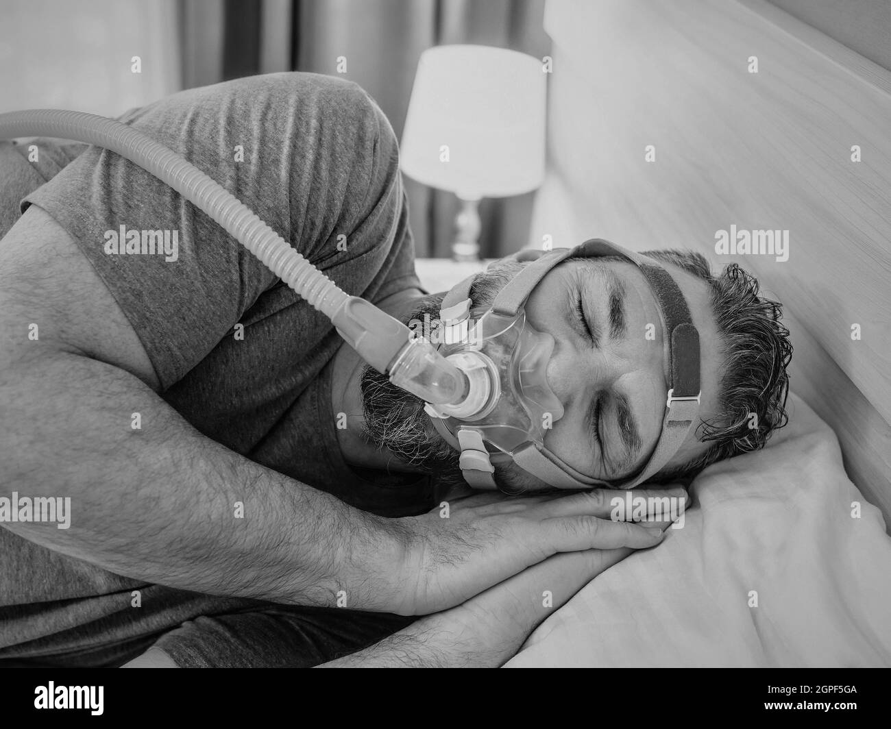 Monochromes Porträt eines schlafenden Mannes mit chronischen Atemproblemen erwägt die Verwendung des CPAP-Geräts im Bett. Gesundheitswesen, obstruktive Schlafapnoe-Therapie Stockfoto