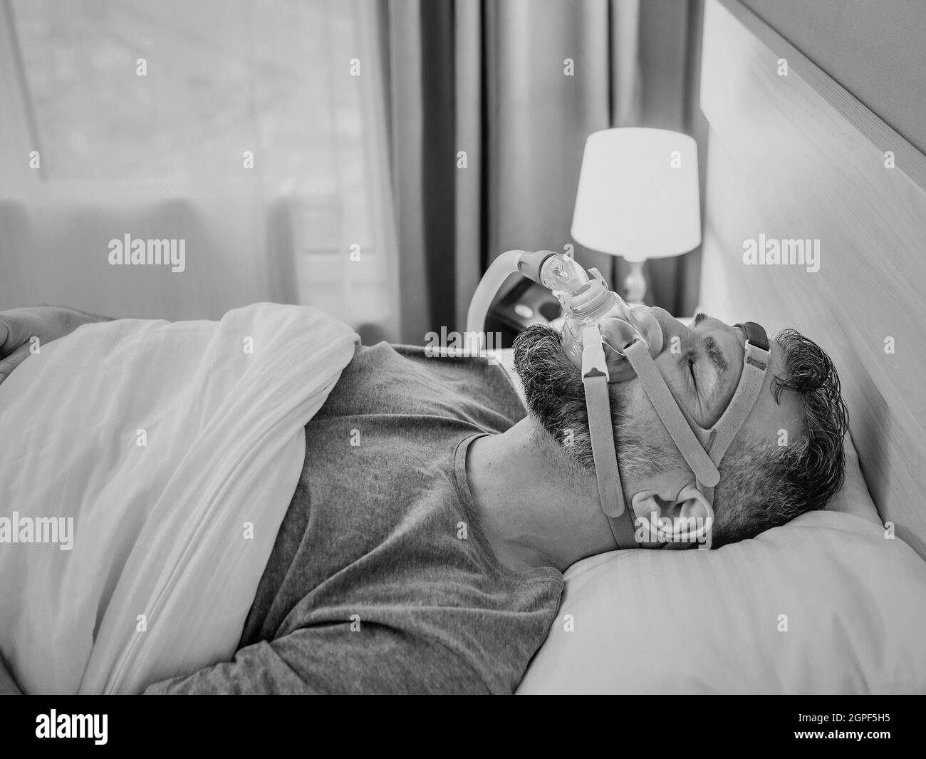 Monochromes Porträt eines schlafenden Mannes mit chronischen Atemproblemen erwägt die Verwendung des CPAP-Geräts im Bett. Gesundheitswesen, obstruktive Schlafapnoe-Therapie Stockfoto