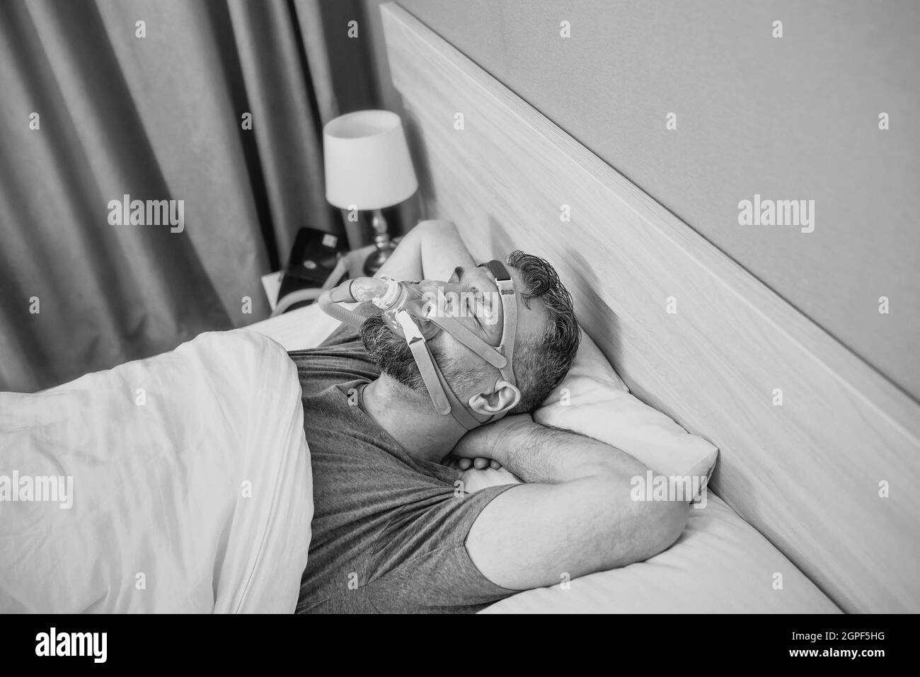 Monochromes Porträt eines schlafenden Mannes mit chronischen Atemproblemen erwägt die Verwendung des CPAP-Geräts im Bett. Gesundheitswesen, obstruktive Schlafapnoe-Therapie Stockfoto