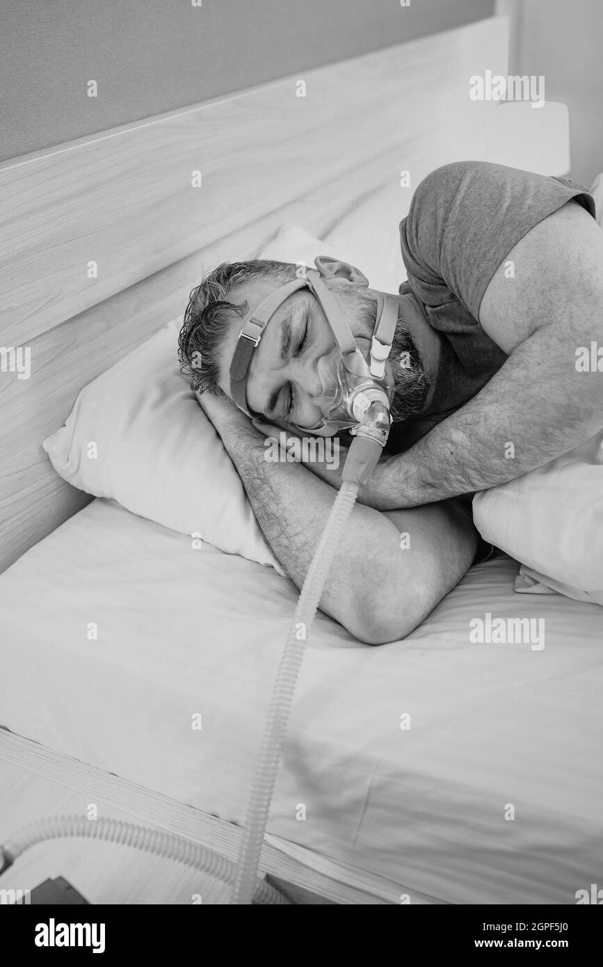 Monochromes Porträt eines schlafenden Mannes mit chronischen Atemproblemen erwägt die Verwendung des CPAP-Geräts im Bett. Gesundheitswesen, obstruktive Schlafapnoe-Therapie Stockfoto