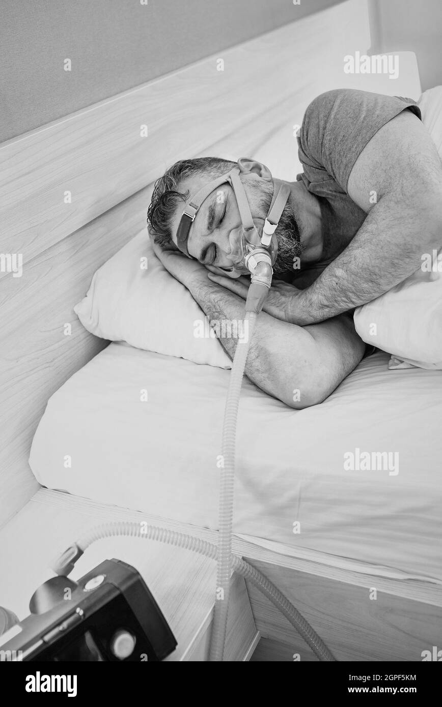 Monochromes Porträt eines schlafenden Mannes mit chronischen Atemproblemen erwägt die Verwendung des CPAP-Geräts im Bett. Gesundheitswesen, obstruktive Schlafapnoe-Therapie Stockfoto