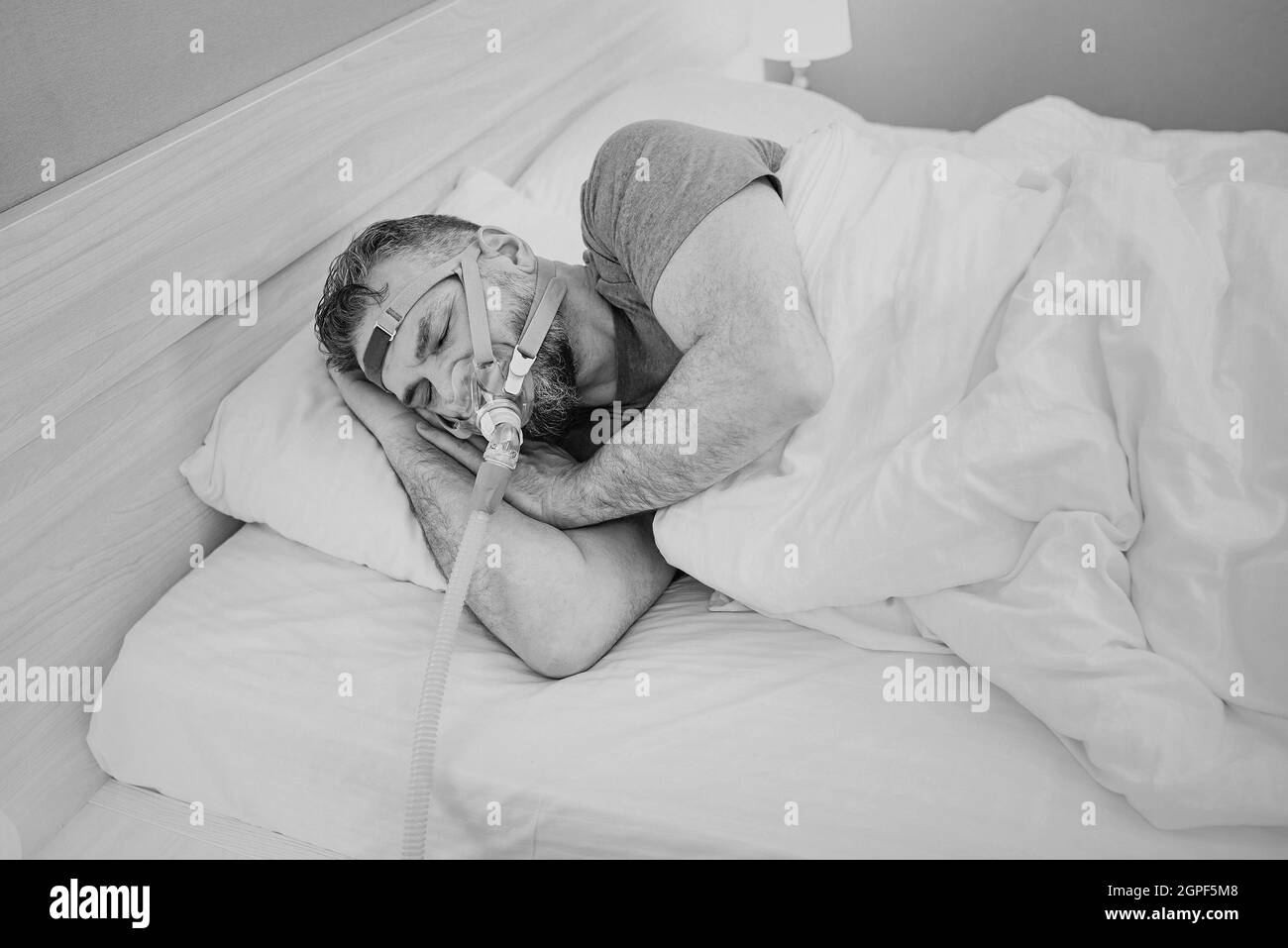 Monochromes Porträt eines schlafenden Mannes mit chronischen Atemproblemen erwägt die Verwendung des CPAP-Geräts im Bett. Gesundheitswesen, obstruktive Schlafapnoe-Therapie Stockfoto