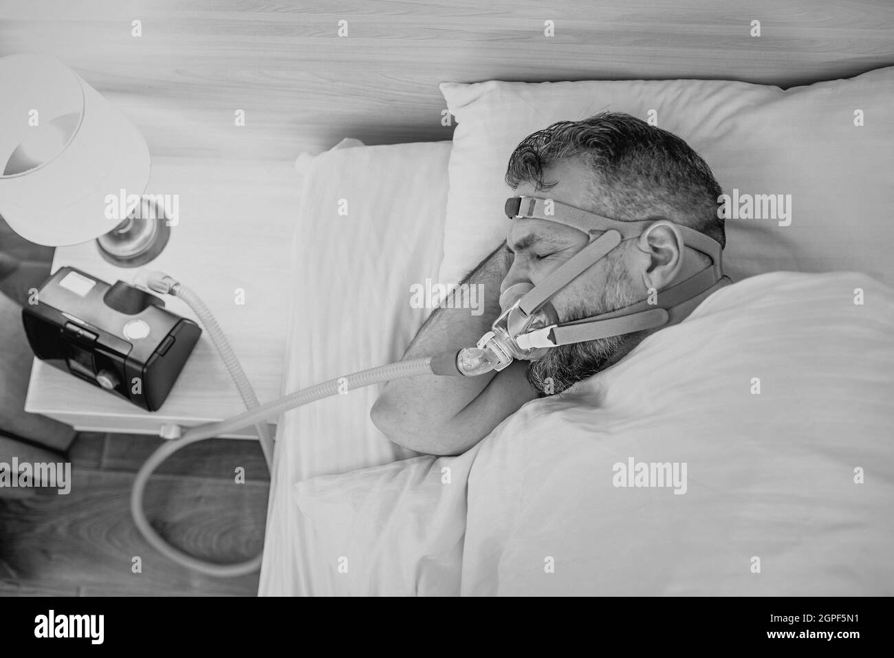 Monochromes Porträt eines schlafenden Mannes mit chronischen Atemproblemen erwägt die Verwendung des CPAP-Geräts im Bett. Gesundheitswesen, obstruktive Schlafapnoe-Therapie Stockfoto