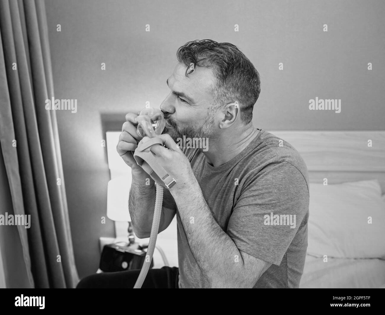 Reifer glücklicher Mann mit chronischen Atemproblemen erwägt die Verwendung CPAP-Maschine auf dem Bett im Schlafzimmer sitzen. Gesundheitswesen, CPAP, Schnarchen Konzept Stockfoto