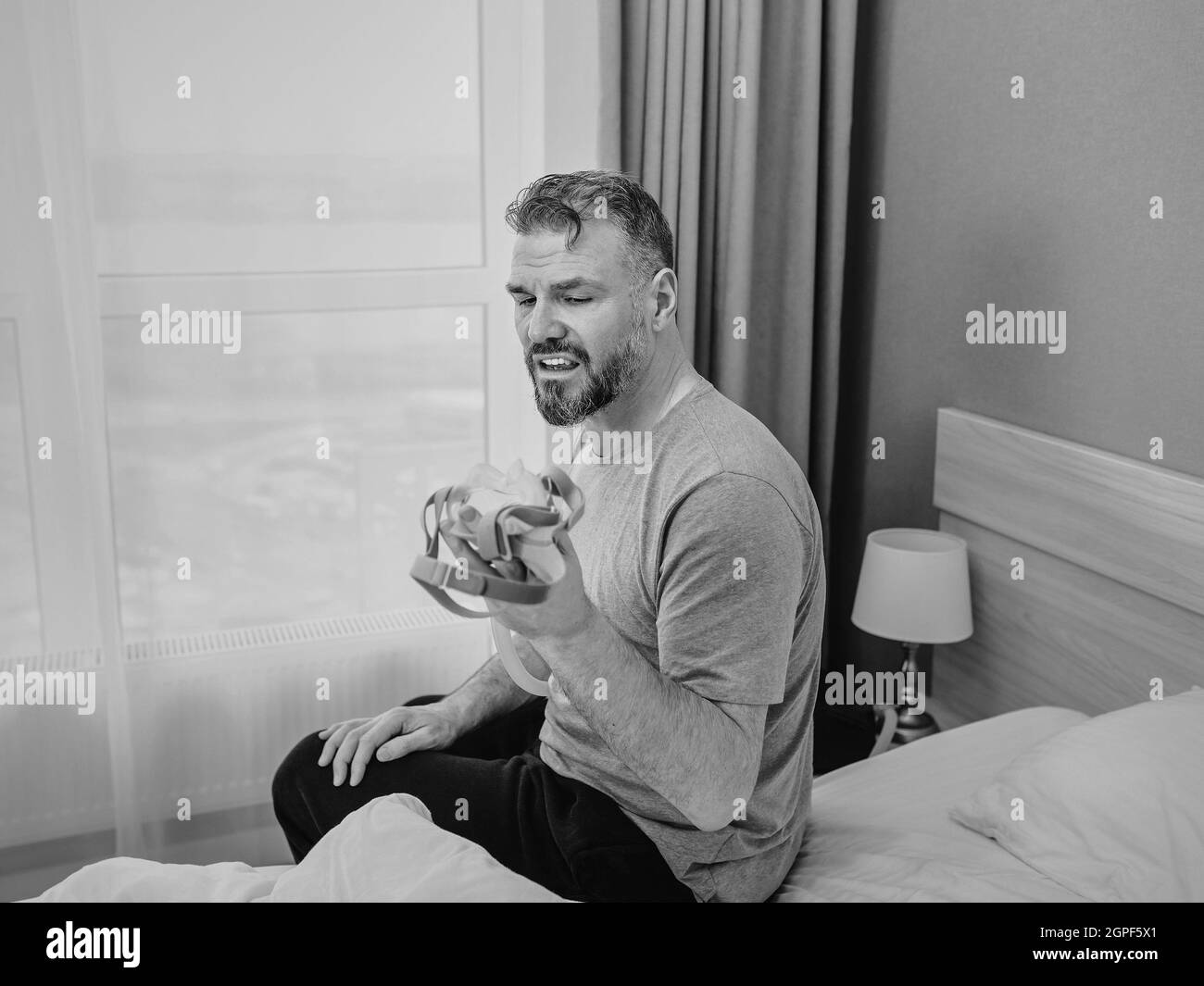 Reifer glücklicher Mann mit chronischen Atemproblemen erwägt die Verwendung CPAP-Maschine auf dem Bett im Schlafzimmer sitzen. Gesundheitswesen, CPAP, Schnarchen Konzept Stockfoto