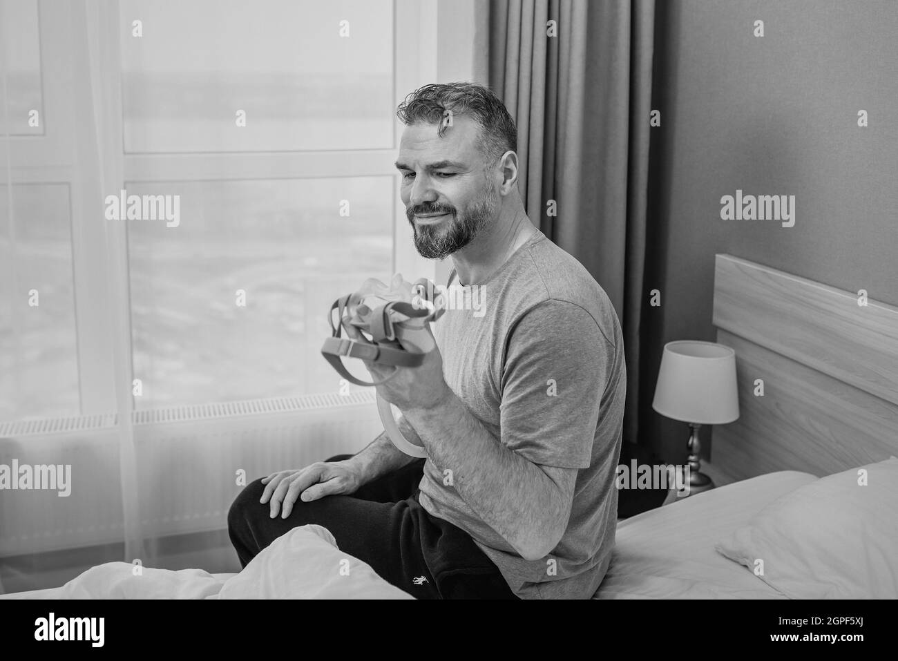 Reifer glücklicher Mann mit chronischen Atemproblemen erwägt die Verwendung CPAP-Maschine auf dem Bett im Schlafzimmer sitzen. Gesundheitswesen, CPAP, Schnarchen Konzept Stockfoto