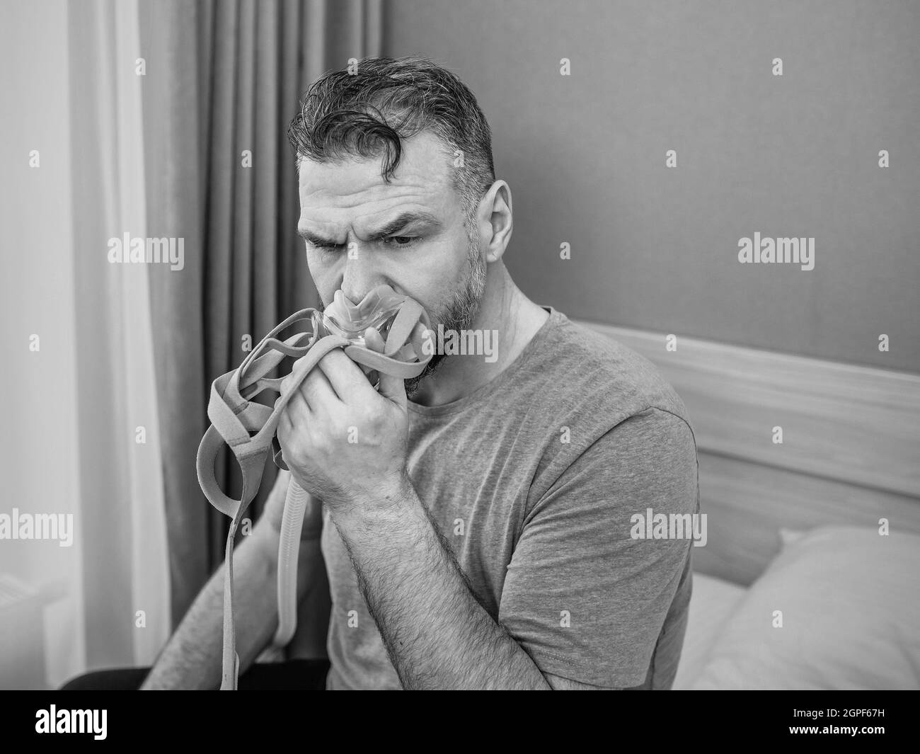 Unglücklich schockiert Mann mit chronischen Atemproblemen überrascht, indem CPAP-Maschine auf dem Bett im Schlafzimmer sitzen. Stockfoto