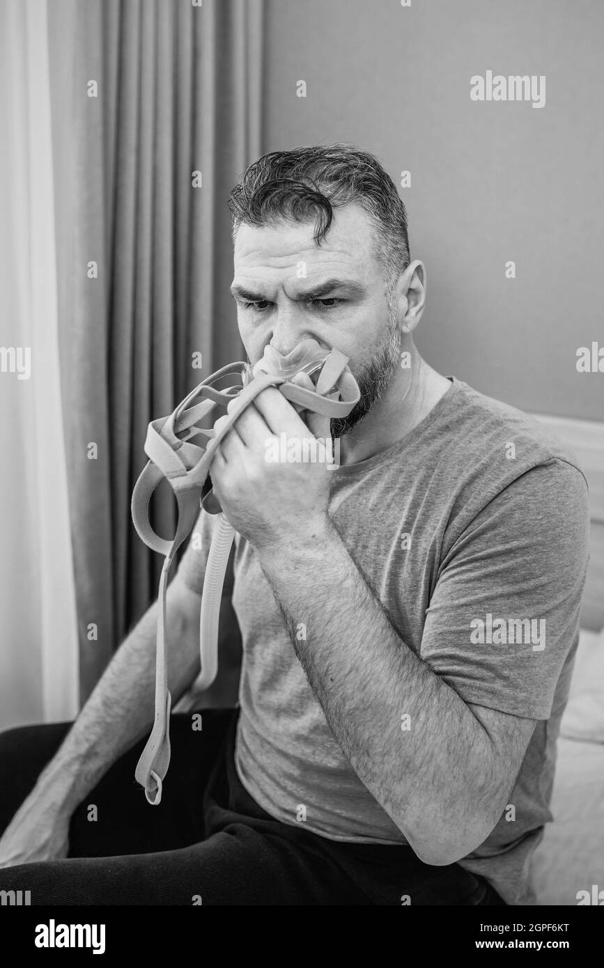 Unglücklich schockiert Mann mit chronischen Atemproblemen überrascht, indem CPAP-Maschine auf dem Bett im Schlafzimmer sitzen. Stockfoto