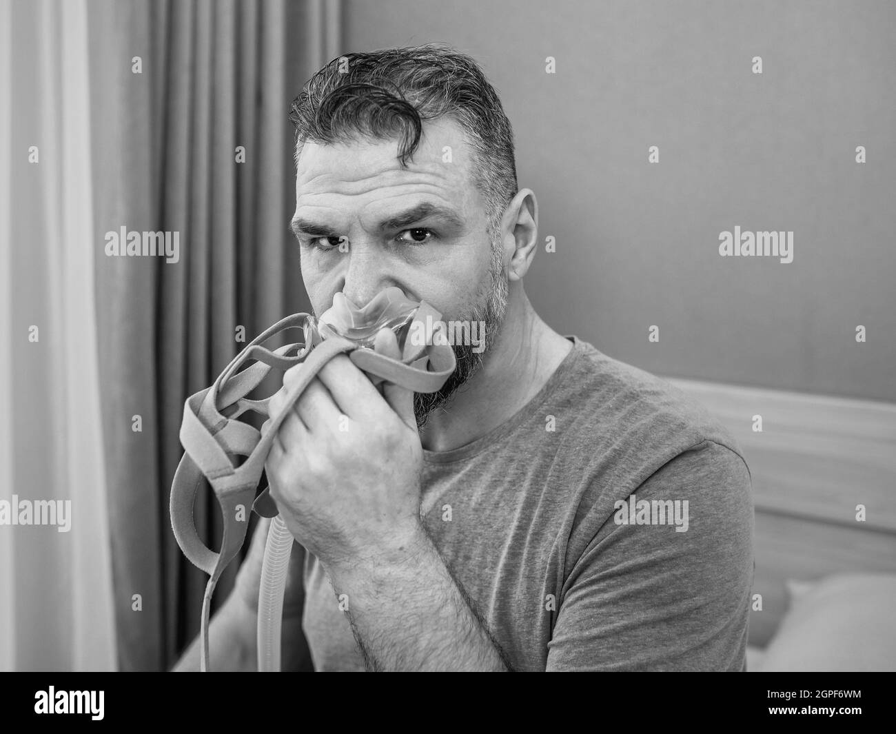 Unglücklich schockiert Mann mit chronischen Atemproblemen überrascht, indem CPAP-Maschine auf dem Bett im Schlafzimmer sitzen. Stockfoto