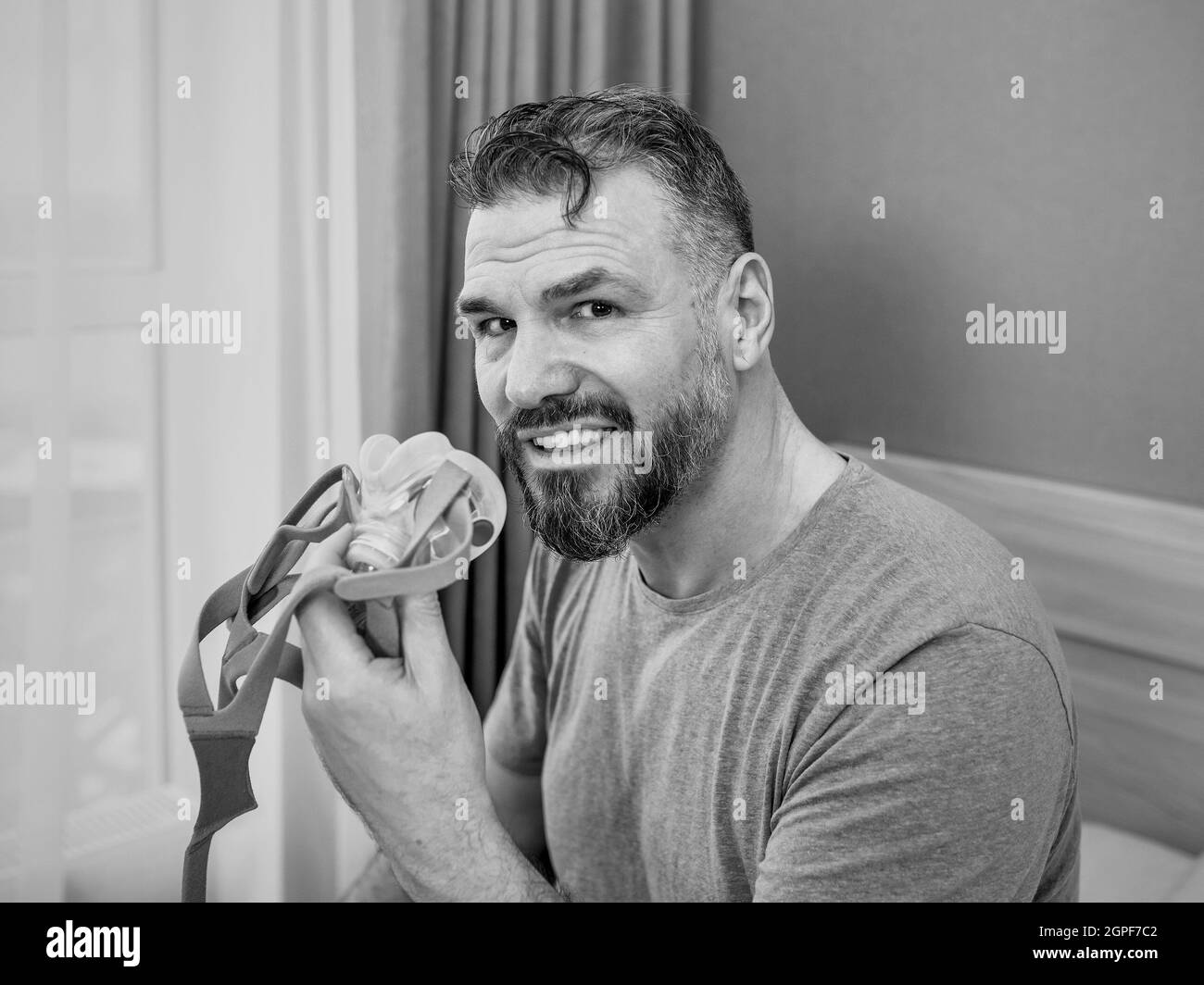 Reifer glücklicher Mann mit chronischen Atemproblemen erwägt die Verwendung CPAP-Maschine auf dem Bett im Schlafzimmer sitzen. Gesundheitswesen, CPAP, Schnarchen Konzept Stockfoto