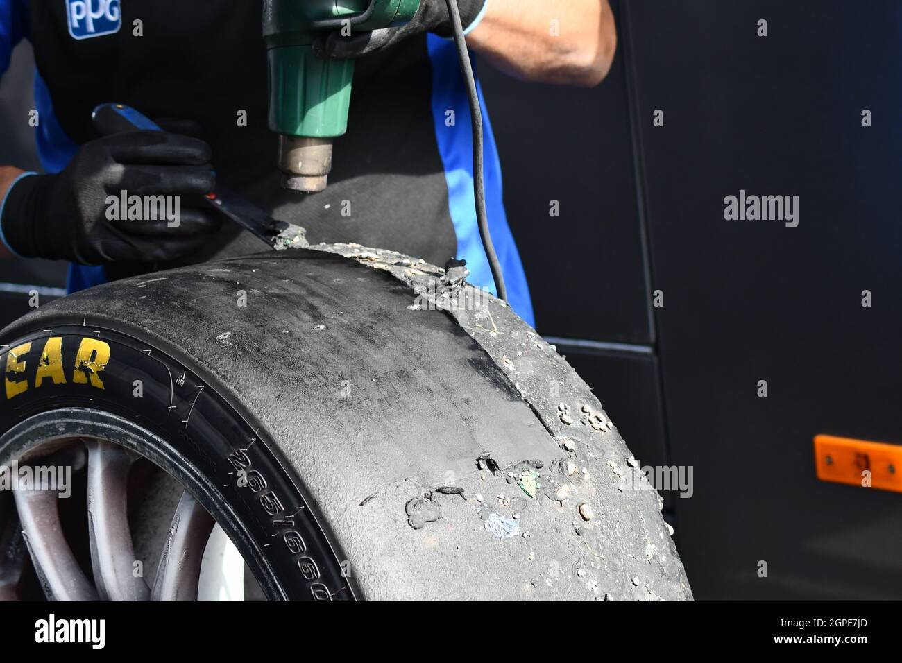 Ein Teammechaniker, der den abgenutzten Gummi mit einer Heißluftpistole aus einem kürzlich ausgefahrenen Rennwagenreifen entfernt Stockfoto