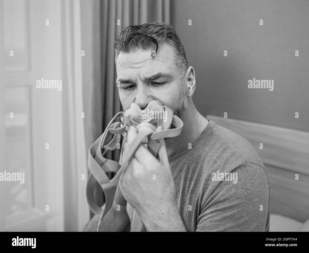 Unglücklich schockiert Mann mit chronischen Atemproblemen überrascht, indem CPAP-Maschine auf dem Bett im Schlafzimmer sitzen. Stockfoto