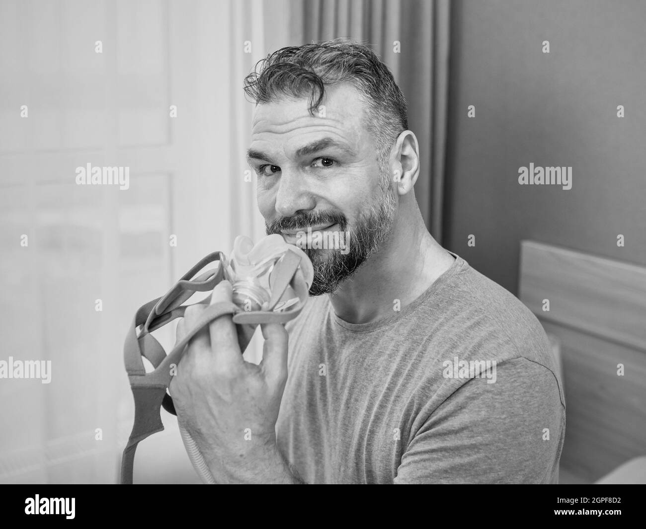 Reifer glücklicher Mann mit chronischen Atemproblemen erwägt die Verwendung CPAP-Maschine auf dem Bett im Schlafzimmer sitzen. Gesundheitswesen, CPAP, Schnarchen Konzept Stockfoto