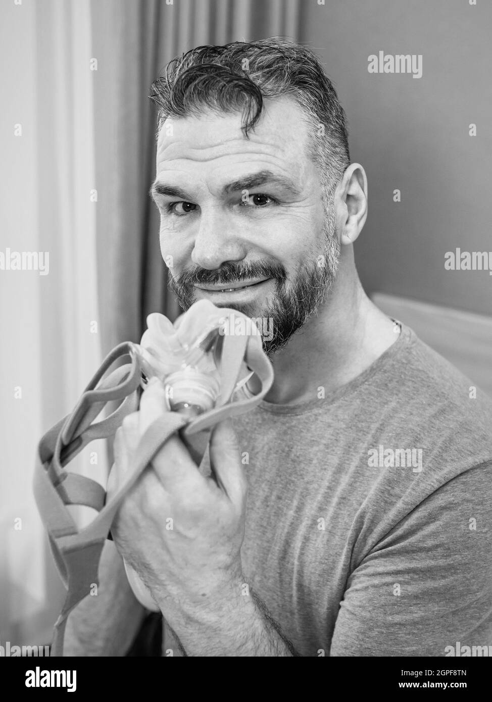 Reifer glücklicher Mann mit chronischen Atemproblemen erwägt die Verwendung CPAP-Maschine auf dem Bett im Schlafzimmer sitzen. Gesundheitswesen, CPAP, Schnarchen Konzept Stockfoto